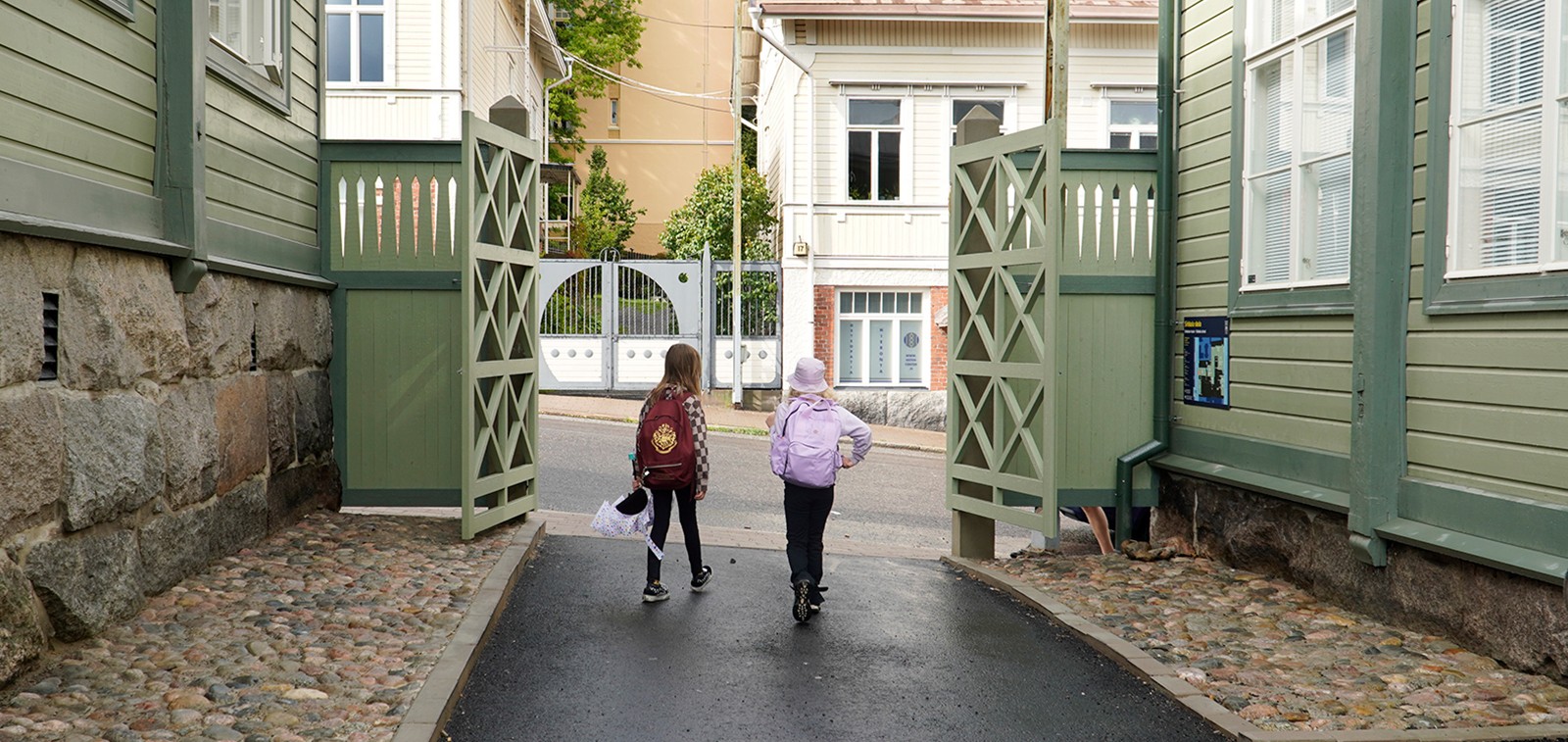 Kaksi tyttöä kulkevat selin ulos koulun pihaporteista.